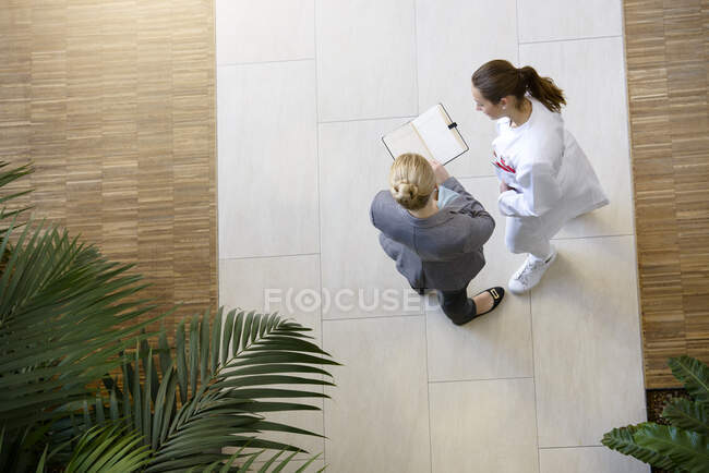 Female doctor and young woman, looking at book, elevated view — Stock Photo