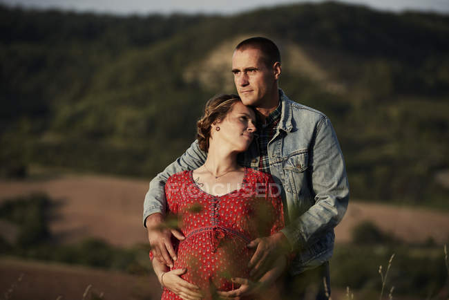Романтичний чоловік з руками на вагітній дружині живіт в ландшафті — стокове фото