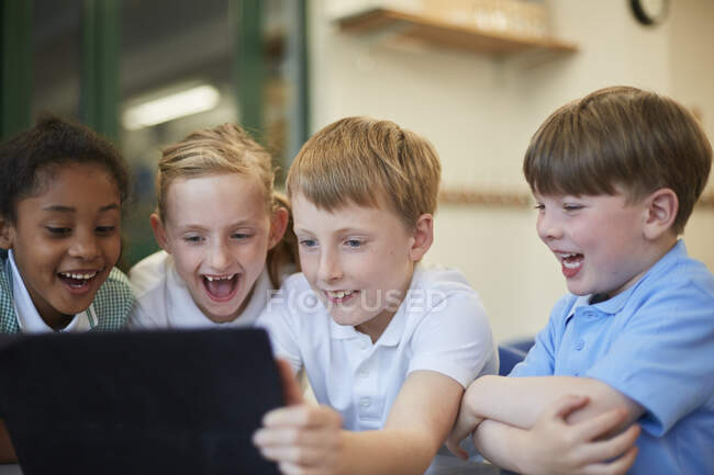 Estudantes e meninas rindo de tablet digital em sala de aula na escola primária — Fotografia de Stock