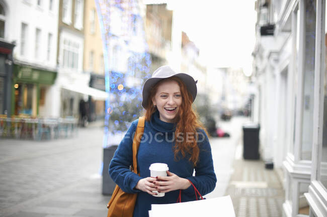 Giovane donna che cammina in strada, con in mano tazza di caffè e shopping bag — Foto stock
