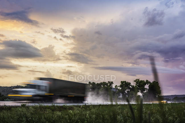 Veículo que viaja na estrada molhada ao pôr-do-sol, Montana, EUA — Fotografia de Stock