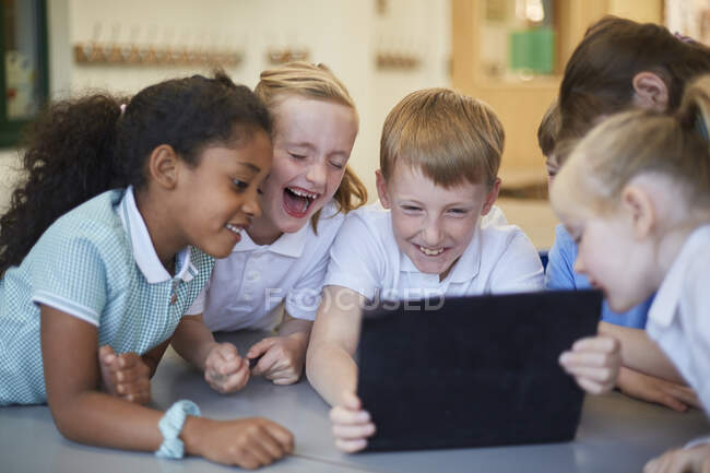 Школьники и девочки смеются над цифровым планшетом в классе в начальной школе — стоковое фото