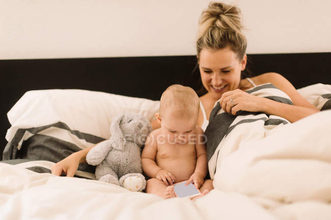 Дитяча дівчинка сидить у ліжку з матір'ю і дивиться на смартфон — стокове фото