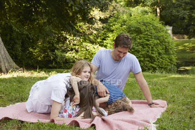 Дорослі батьки з двома дочками схилилися до пікнікового ковдру в парку. — стокове фото