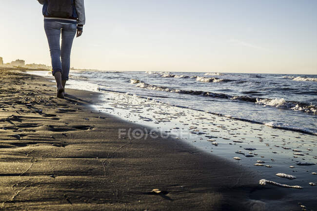 Vue de la taille vers le bas de la femme pieds nus se promenant le long du bord de l'eau sur la plage, Riccione, Emilie-Romagne, Italie — Photo de stock