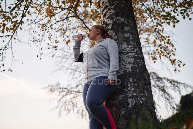 Curvaceous jovem mulher formação e beber água engarrafada no parque — Fotografia de Stock