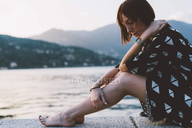 Молодая женщина сидит на набережной у озера Комо, Ломбардия, Италия — стоковое фото