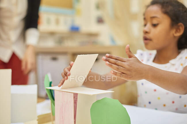 Primary schoolgirl making cardboard structure on classroom desk — Stock Photo