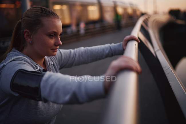 Изогнутая молодая женщина, прислонившаяся к перилам пешеходного моста в сумерках — стоковое фото