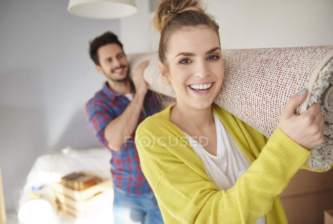 Young couple carrying rolled carpet on shoulders — Stock Photo