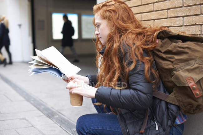 Junge Frau sitzt draußen, hält Kaffeetasse in der Hand, schaut auf Landkarte — Stockfoto