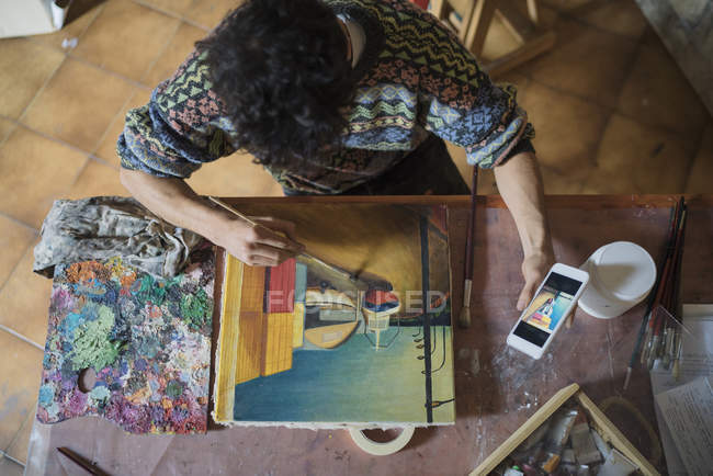 Artista che guarda smartphone mentre dipinge su tela in studio — Foto stock