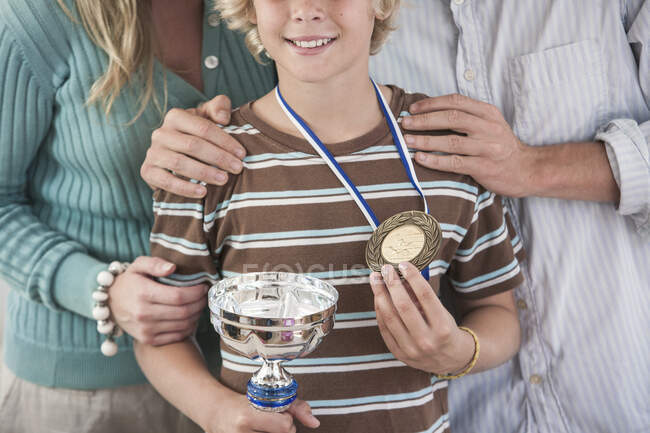 Vista ritagliata del ragazzo che tiene orgogliosamente trofeo e medaglia — Foto stock