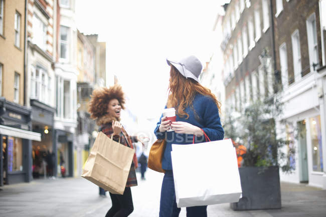 Dos mujeres jóvenes con bolsas saltándose unas a otras en la calle - foto de stock