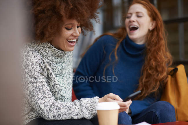 Друзі в кав'ярні використовують мобільний телефон і сміються — стокове фото