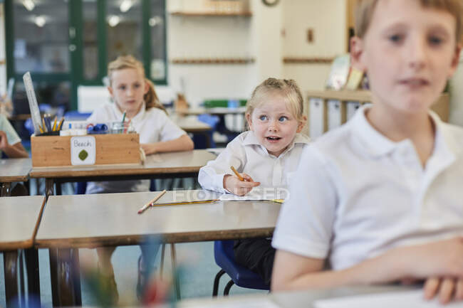 Alunas primárias e menino fazendo trabalhos escolares em mesas de aula — Fotografia de Stock