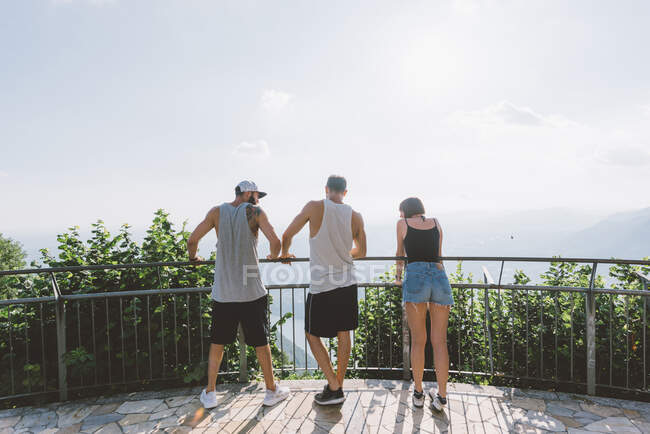 Vue arrière de trois jeunes amis adultes regardant le lac de Côme depuis le balcon, Côme, Lombardie, Italie — Photo de stock