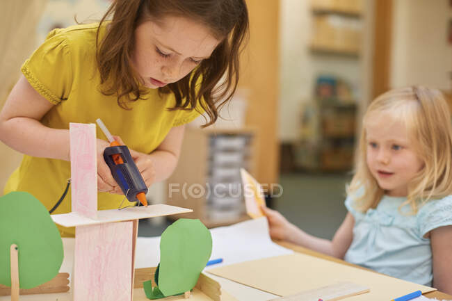 Primary schoolgirls making cardboard model at classroom desk — Stock Photo