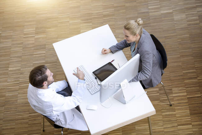 Мужчина врач и молодая женщина сидят за столом, обсуждают, возвышенный взгляд — стоковое фото