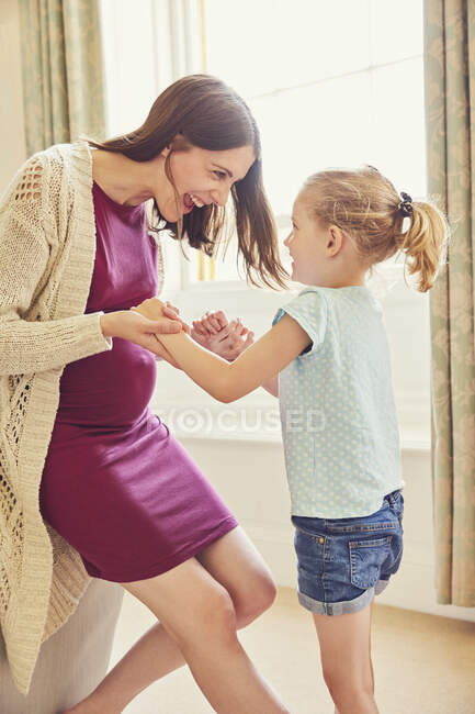 Сміється вагітна жінка грає з дочкою у вітальні — стокове фото