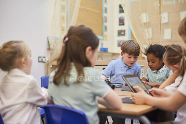 Школярі і дівчата дивляться на цифрові планшети в класі в початковій школі — стокове фото