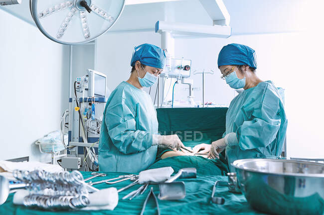 Cirurgiões que realizam cirurgia no abdômen do paciente na sala de cirurgia da maternidade — Fotografia de Stock