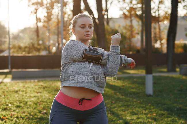 Kurvige junge Frau trainiert im Park und streckt die Arme aus — Stockfoto