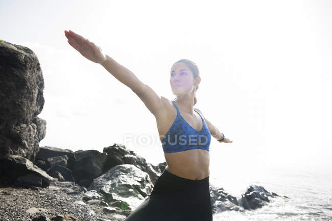 Young woman in warrior yoga pose on beach — Stock Photo
