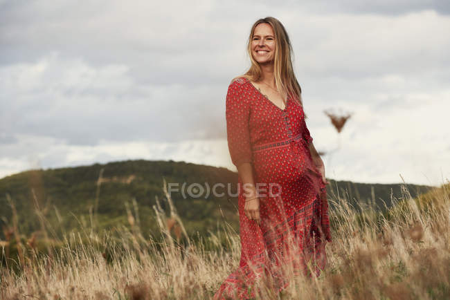 Portrait of happy pregnant woman in red dress on hillside — Stock Photo
