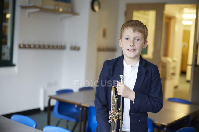 Estudiante de primaria sosteniendo trompeta en el aula, retrato - foto de stock