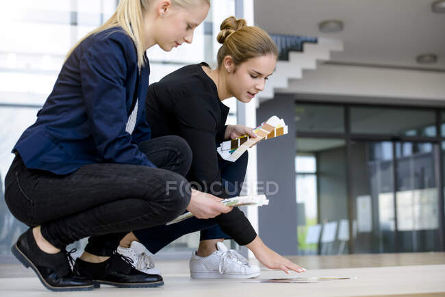 Two young businesswomen crouching on office floor discussing colour swatches — Stock Photo