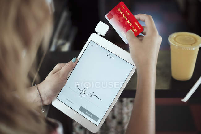 Vista sobre el hombro de una mujer joven sosteniendo tableta digital y tarjeta de crédito - foto de stock