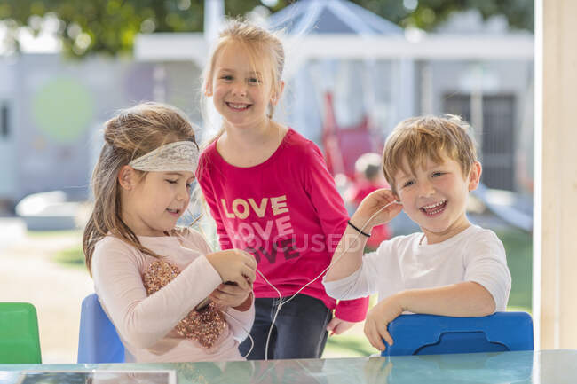 Young girl outdoors with friends, holding smartphone, sharing earphones — Stock Photo