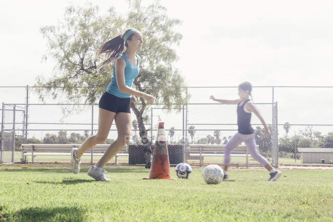 Studentesse che fanno pratica pallone da calcio dribbling sul campo sportivo scolastico — Foto stock