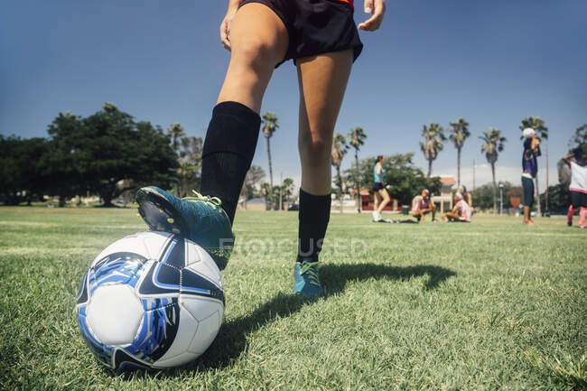 Талия юной школьницы футболистки с ногами на мяче на школьной спортивной площадке — стоковое фото