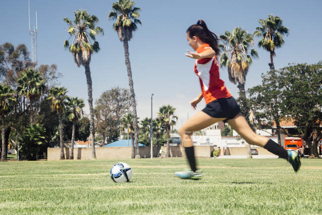 Adolescente escolar corriendo a patear pelota de fútbol en el campo de deportes de la escuela - foto de stock