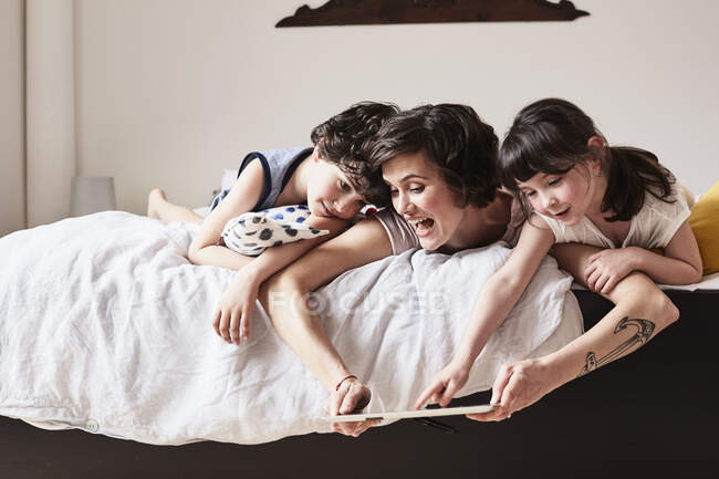 Мать, сын и дочь лежат на кровати, используя цифровой планшет — стоковое фото