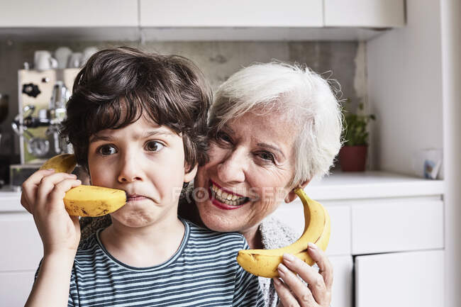 Grandmother and grandson fooling around, using bananas as telephones, laughing — Stock Photo