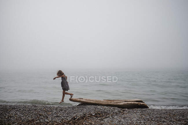 Girl on beach playing on driftwood — Stock Photo