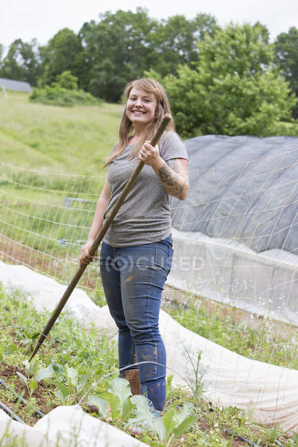 Woman holding hoe and smiling at camera in vegetable garden — Stock Photo
