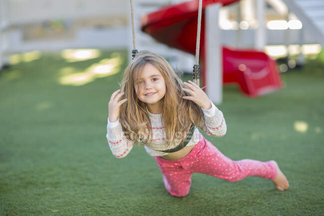 Девочка в детском саду, портрет лежащий на качелях в саду — стоковое фото