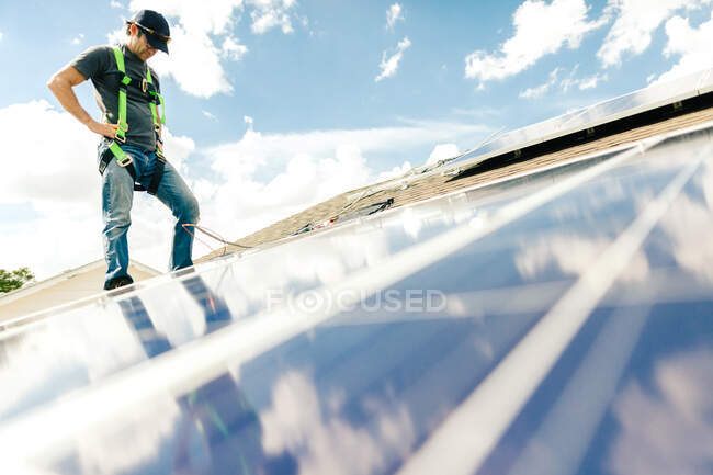 Робітник стоїть на даху будинку, встановлюючи сонячні батареї. — стокове фото