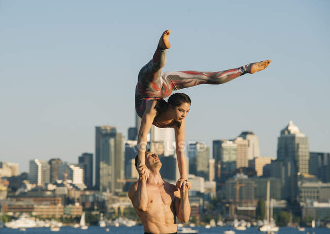 Adolescente y joven, al aire libre, mujer balanceándose en las manos del hombre en posición de yoga - foto de stock