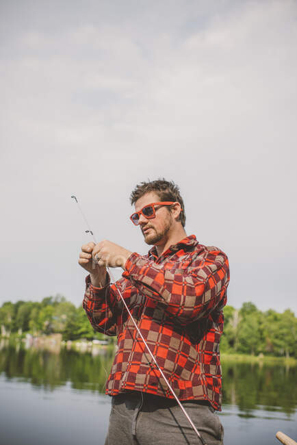 Young man on lake, preparing fishing line — Stock Photo