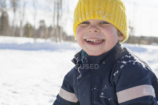 Retrato de menino feliz em chapéu de malha amarelo na neve paisagem coberta — Fotografia de Stock