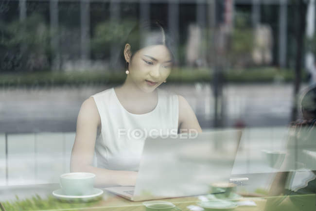 Femme d'affaires assise dans un café et utilisant un ordinateur portable, vue par la fenêtre — Photo de stock