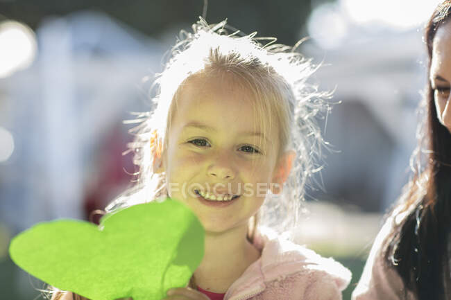 Young girl outdoors, holding green paper heart, smiling — Stock Photo