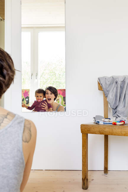 Mãe e bebê filha olhando no espelho, visão traseira — Fotografia de Stock