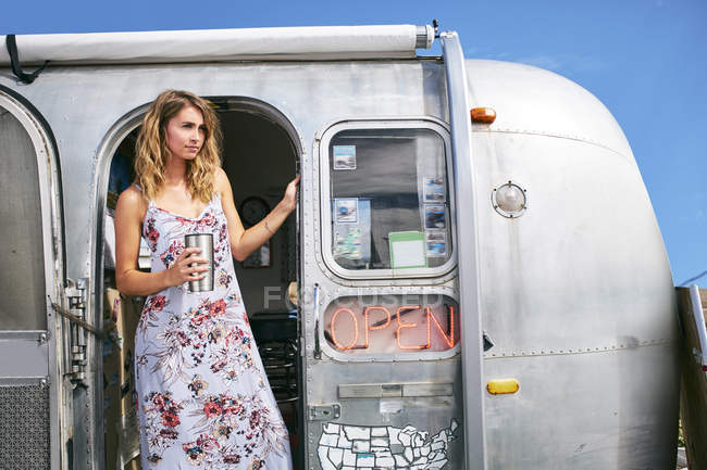 Young woman with coffee looking out from airstream  coffee shop doorway — Stock Photo