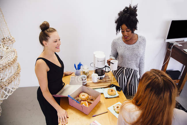 Колеги в кав'ярні, що розділяє коробку з пончиками — стокове фото